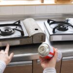 古いカセットコンロの製造表示と買い替え用本体、カセットボンベを確認する様子