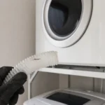 衣類乾燥機の前でひび割れた排水ホースを確認している様子