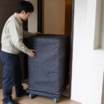 養生した重い金庫を狭い玄関から搬入する場面