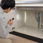キッチンのシンク下で電源と設置空間を確認する様子