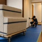 養生したアップライトピアノの搬入前に扉と通路を採寸する作業者