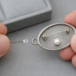 チェーン端部とブローチ裏の通し金具を照合する手元