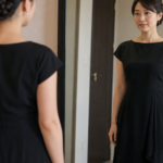 鏡の前で黒いドレスの胸元と背中を確認する女性