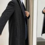 鏡の前でダークカラーのチェスターコートのサイズ感を確かめる人物