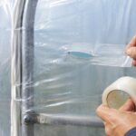 ビニールハウスの破れに透明な補修テープを貼っている様子