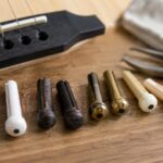 アコースティックギターのブリッジと複数種類のブリッジピンを並べたイメージ