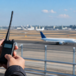 空港の展望デッキで受信機を持ち、滑走路の旅客機を見ている様子