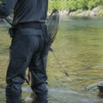 鮎釣り用の腰ベルトにタモと引舟を取り付けて川に立つ釣り人