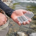 川辺で釣り用ベストから針ケースを取り出す手元