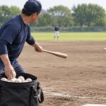 野球コーチがボールバッグから球を取り出してノックする様子