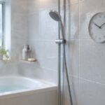 水滴の付いた浴室の壁に丸い時計が掛かっている様子