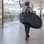 駅構内で自転車を収めた輪行袋を肩に掛けて運ぶ人