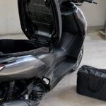 シート下収納を開けたスクーターと横に置かれた柔らかいバッグ
