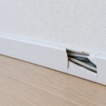 壁際で割れて内部のコードが見えている白い配線モール