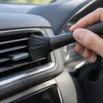 車のエアコン吹き出し口を柔らかなブラシで掃除している様子
