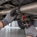 車体下の排気管にチェーン式の切断工具を当てる整備風景