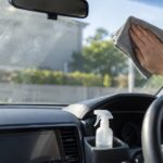 車の内側からフロントガラスの汚れをクロスで拭いている様子