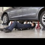 リジッドラックで支えた車の下で整備クリーパーを使う作業者