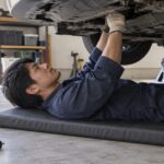 車体の下でクッションマットに横たわり整備する作業者