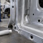 車体パネルの継ぎ目と無地のシームシーラー容器が並ぶ整備工場の様子