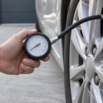 車のタイヤにホース付き空気圧ゲージを接続して測定している様子