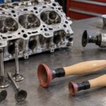車のシリンダーヘッドと複数のバルブすり合わせ工具を整備台に並べた様子