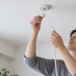 天井の照明接続部と電源コードを手にする人物