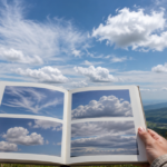 山の上で雲の写真図鑑を開き、空の雲を観察している様子