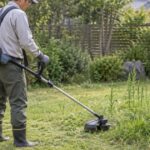 住宅の庭で充電式刈払機を使って草を刈る人