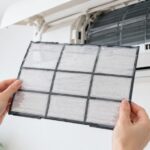 壁掛けエアコンの前でフィルターを手に持っている様子