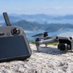 山と水辺を背景にドローンと画面付き送信機を並べたイメージ