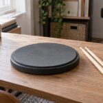 木製机に丸いドラム練習用パッドとスティックを置いた自宅練習の風景