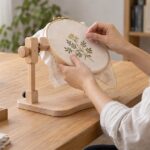 木製の卓上スタンドに固定した刺繍枠へ両手で刺繍している様子