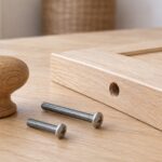 木製の家具扉とつまみ、長さの異なる2本のねじを並べた様子