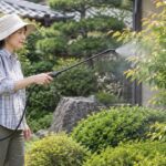 肩掛け式の噴霧器で庭木に霧を散布している様子