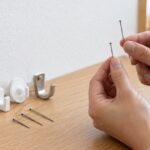 石膏ボード壁の前で長さの異なるピンと壁掛けフックを比べている様子