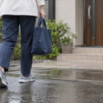雨上がりの住宅へ向かう訪問介護員とワークシューズ