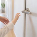室内ドアのレバーハンドルへ手を伸ばす幼児を大人が見守る様子