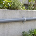 庭のコンクリート壁にサドルで固定された灰色の散水用塩ビ管