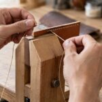 木製の固定具で革を挟み、両手で手縫いしている様子