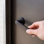 玄関ドアのレバーハンドルの緩みを手で確かめている様子