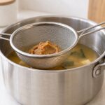 鍋の上に味噌を入れたステンレス製の味噌こしを掛けている様子