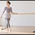 自宅で自立式バレエバーに手を添えて練習する女性