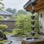 雨の日の住宅軒先でカップ式の雨水鎖を水が流れる様子