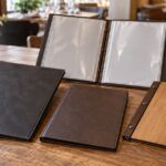 飲食店のテーブルに大きさや表紙素材が異なるメニューブックを並べた様子
