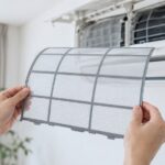 壁掛けエアコンの前でエアーフィルターを手に持っている様子
