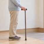 玄関で一本杖のグリップに手を添えて立つ高齢者