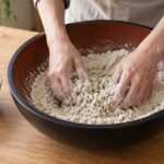 大きなこね鉢でそば粉を両手で混ぜている様子
