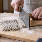 麺切り包丁と駒板を使ってそば生地を切っている様子
