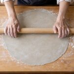 木製ののし板でそば生地を麺棒で延ばしている様子